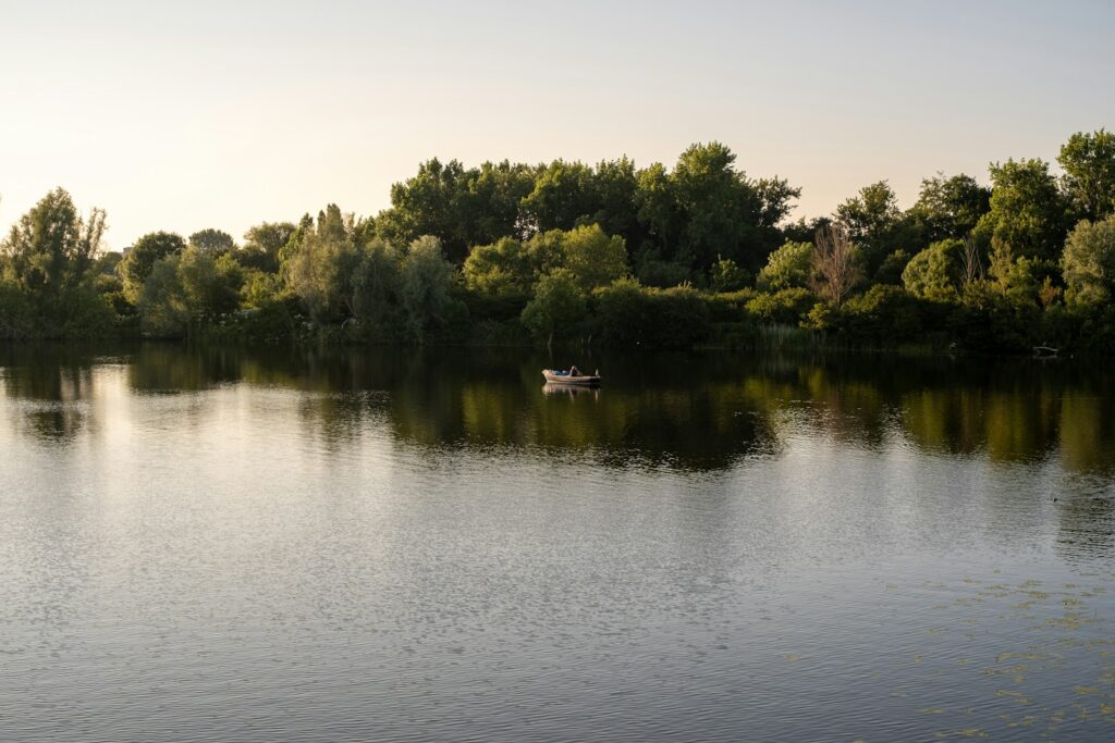 A calm lake reflects trees and a boat.